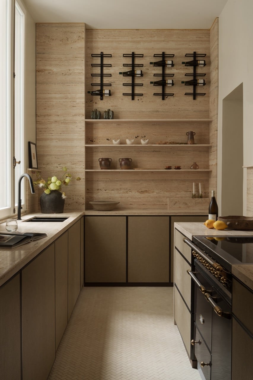 The kitchen features light travertine with grey stripes, creating visual continuity throughout the Parisian apartment, complemented by custom wine storage and built-in shelving