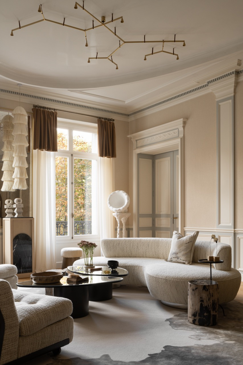 The living room showcases the preserved original plasterwork enhanced with LED lighting, custom boucle seating, and the branch-like chandelier installation that references “curved ceilings of Parisian palaces,” all designed to accommodate entertaining while maintaining intimate conversation areas