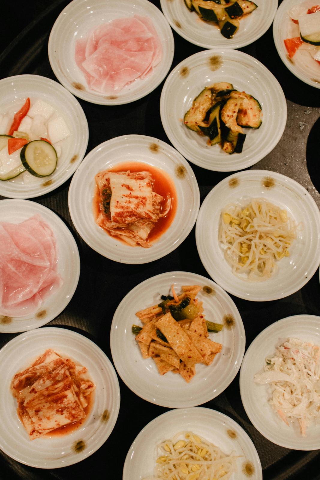 A Korean dining table with multiple banchan side dishes including kimchi and vegetables