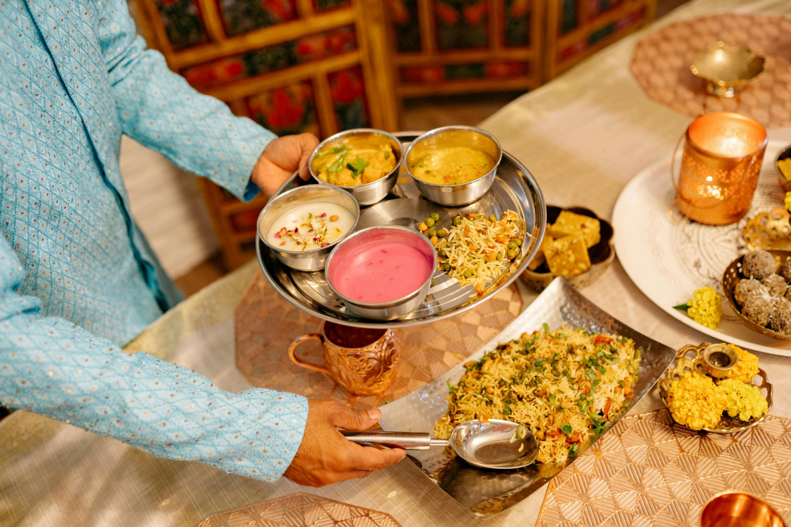 A person serving an Indian thali platter with rice, dal, vegetables, chutneys and sweets
