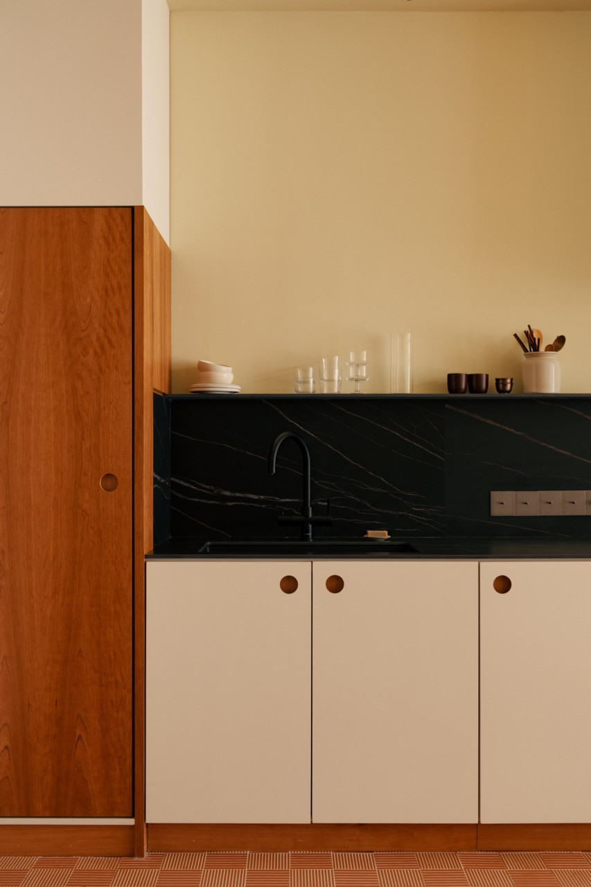 Kitchen cabinet handles are designed as circular recesses that contrast with the grid pattern of the terracotta flooring