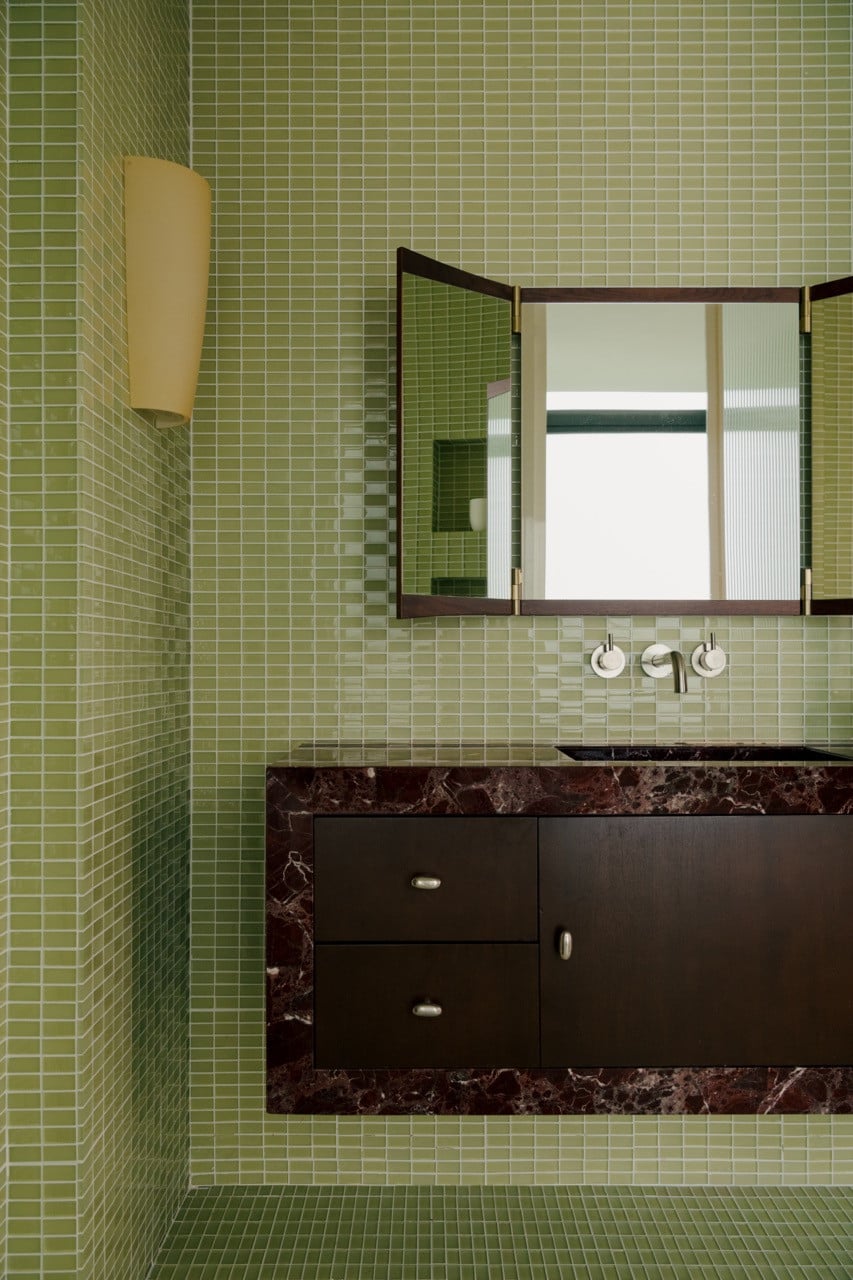 The GUBI bathroom mirror was chosen specifically for how its unique shape works with the gridded mosaic, whilst dark timber vanity drawers are integrated into the marble countertop