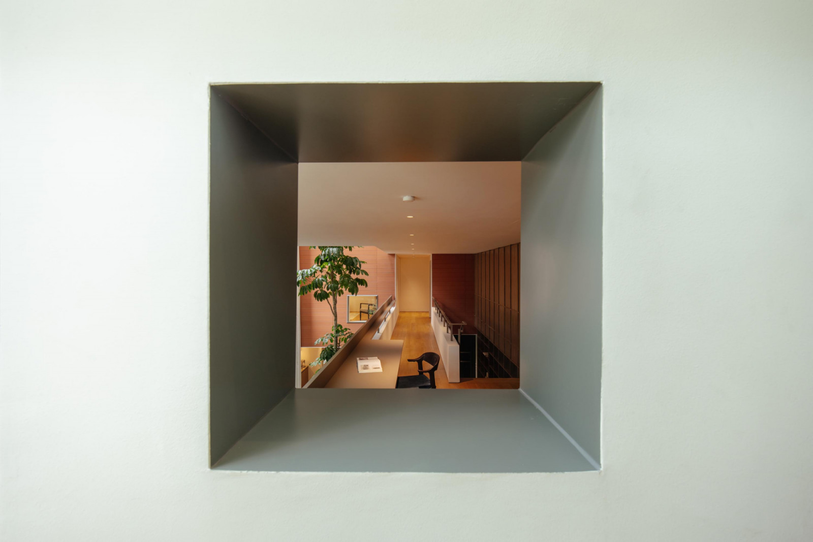 A square picture window offers a warm-toned layered view across the semi-detached home’s atrium