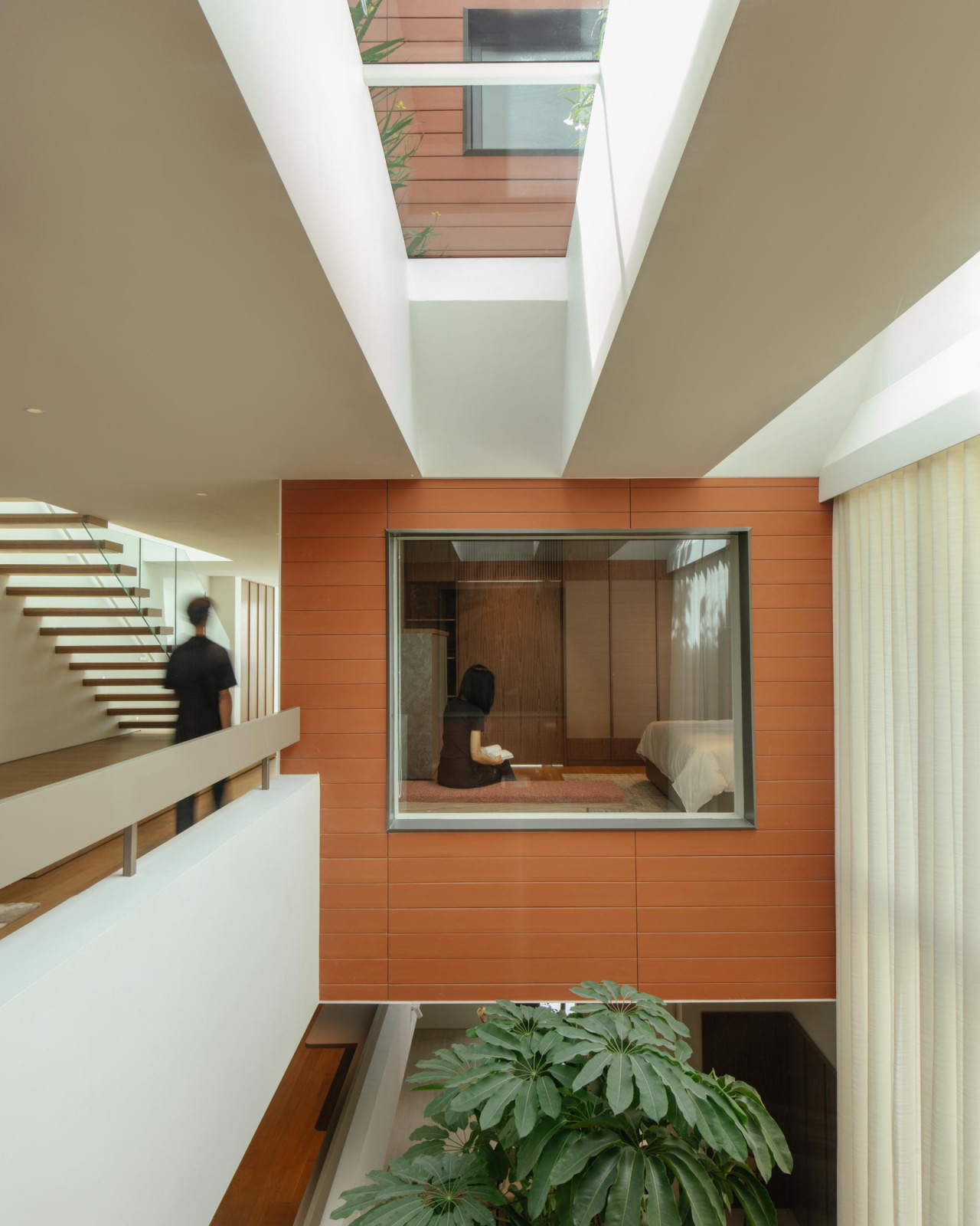 From the atrium, a bedroom’s picture window opens to views of the tree canopy and the layered volumes beyond, with ample daylight courtesy of the skylight