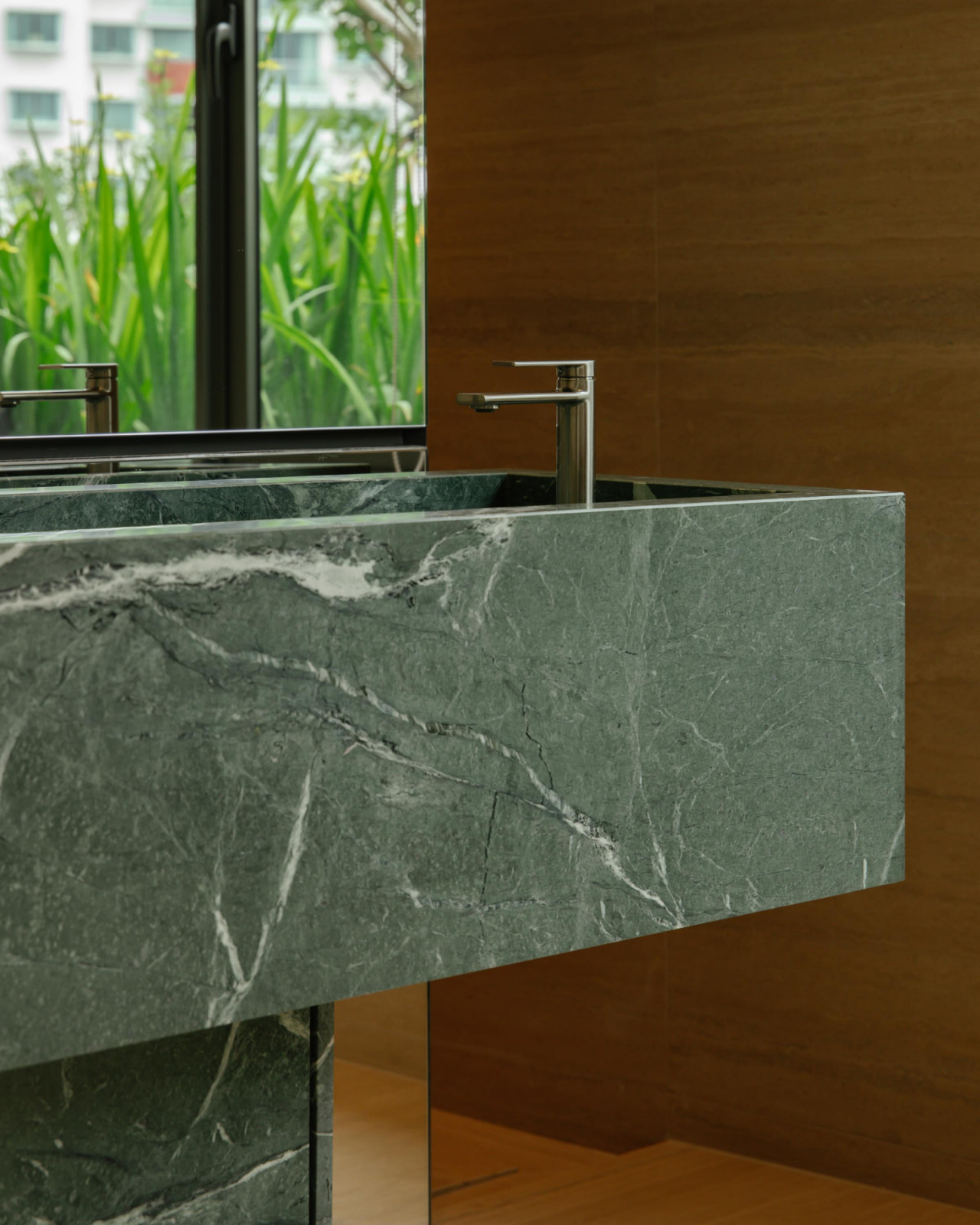This bathroom’s green marble vanity adds a striking pop of colour, its veining set against warm timber walls and views of lush planting outside