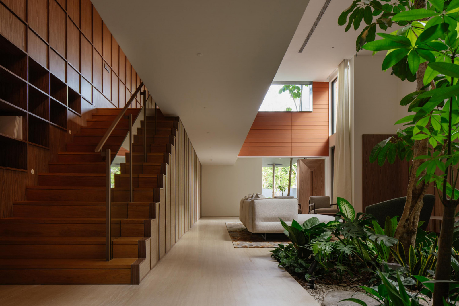 The staircase and surrounding carpentry function as a single timber-clad object, its crisp geometry softened by indoor greenery