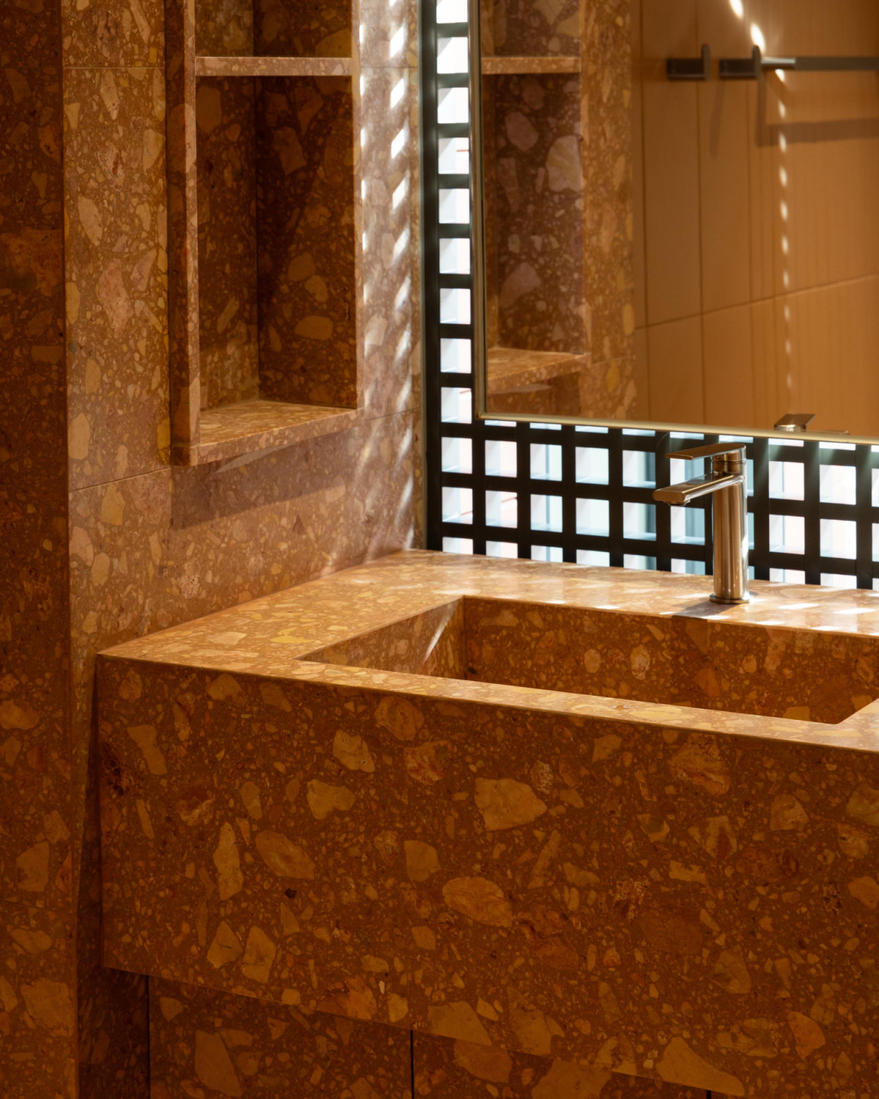 In the bathroom, warm-toned terrazzo sink and shelving’s flecked surface adding depth and texture