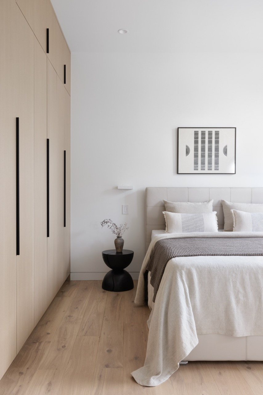 A bedroom features floor-to-ceiling built-in wardrobes with black linear hardware, maximising storage within the clean aesthetic maintained throughout the home’s four bedrooms