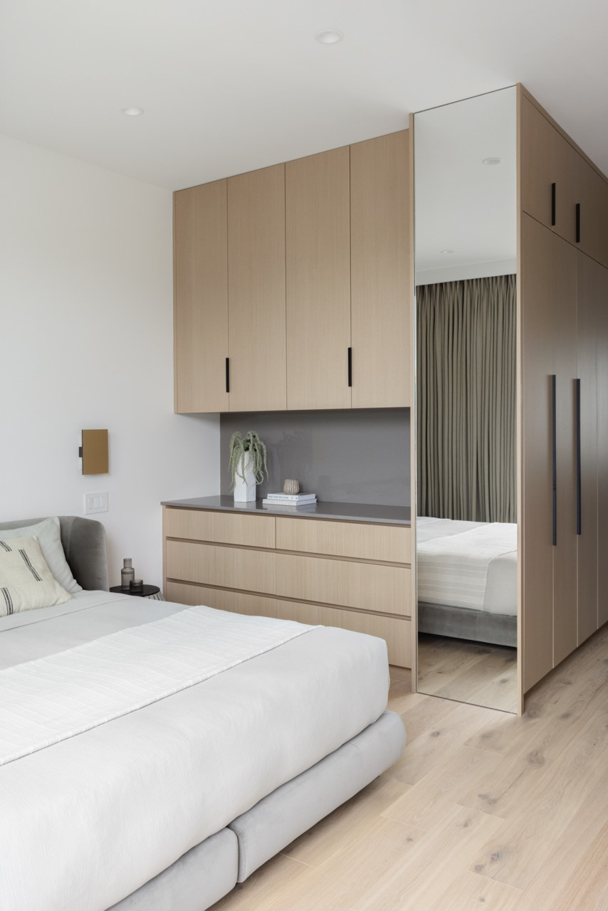 Custom millwork in the primary bedroom provides extensive storage while maintaining the home's consistent material palette of light wood tones and clean, modern detailing