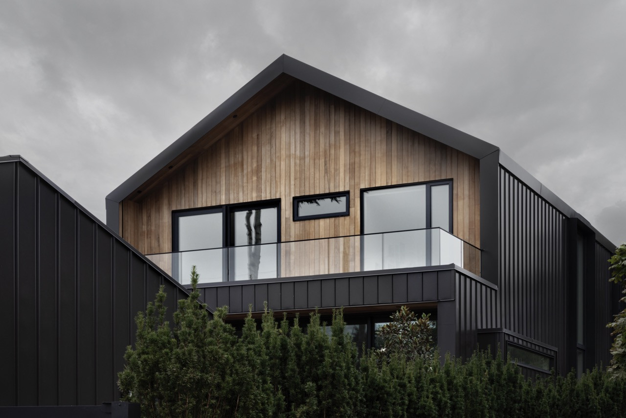 The rear balcony extends the living space outdoors, with the cedar-clad upper level cantilevering over the dark metal-clad ground floor to create protected outdoor areas