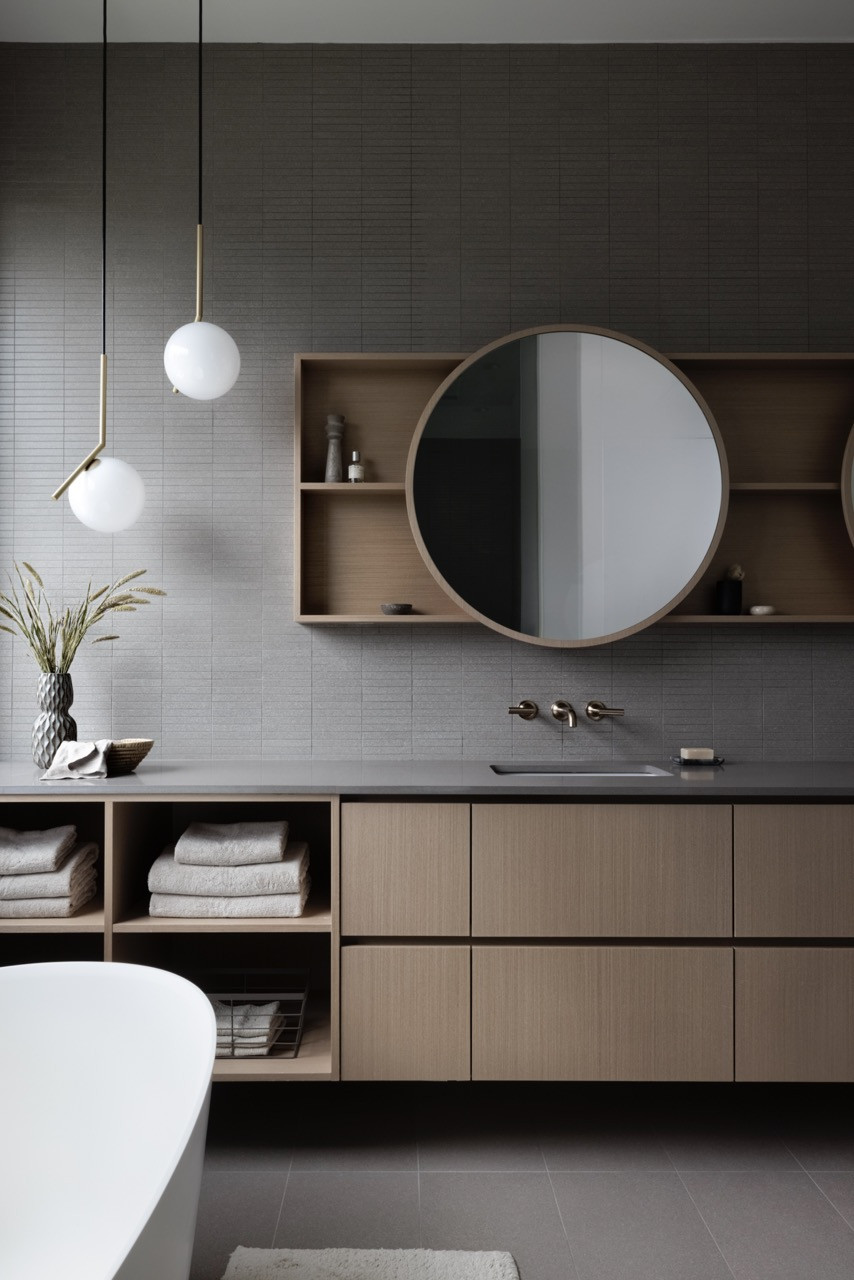 The primary bathroom includes a floating double vanity with integrated storage and circular mirrors, maintaining the home’s material consistency with wood cabinetry and grey tile finishes