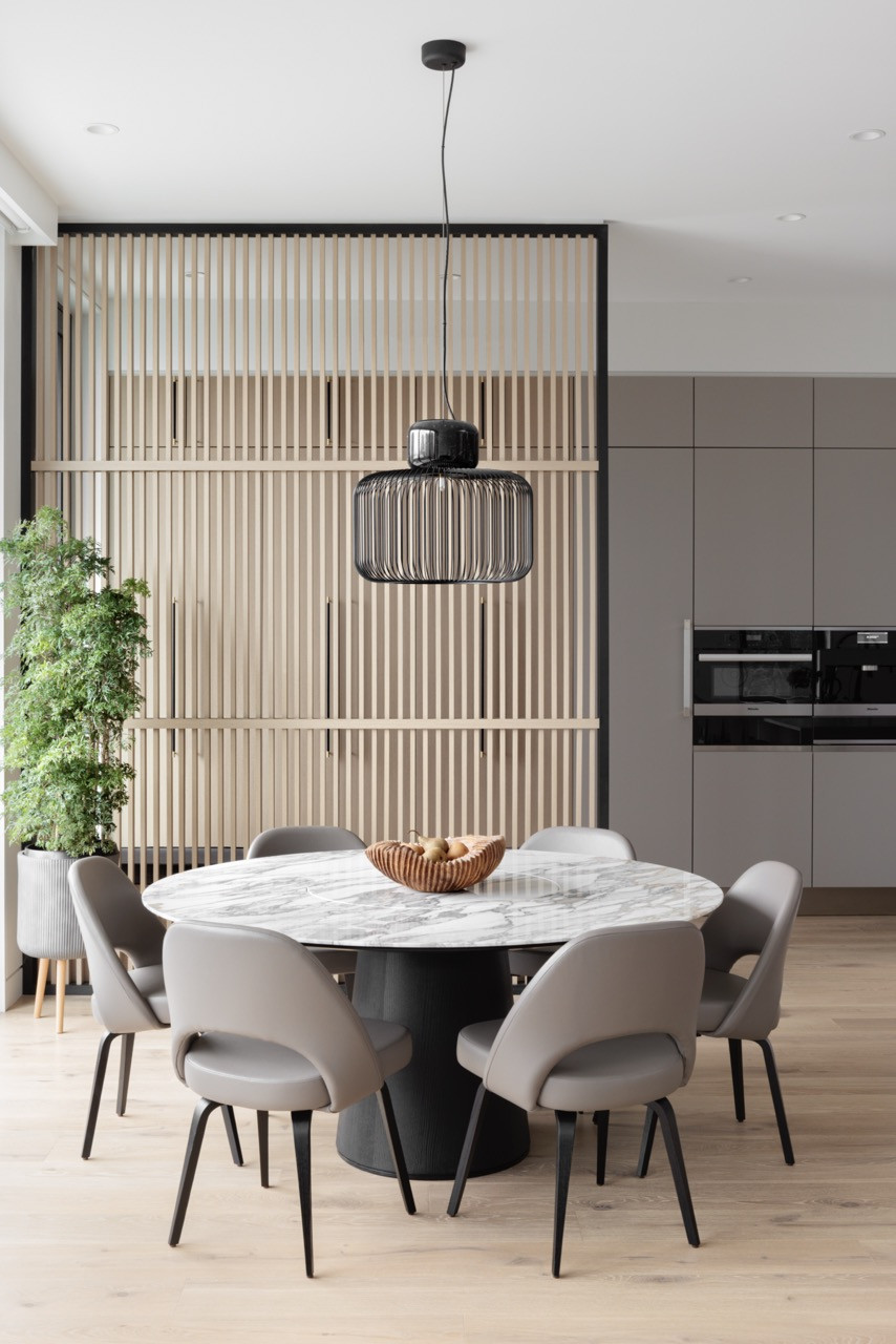 The dining table features the Porro Materic design with Knoll Saarinen chairs, positioned to take advantage of natural light while the wood slatted wall provides visual warmth and cultural reference
