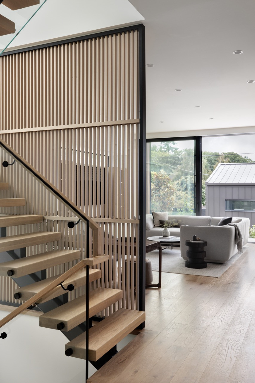 The central staircase features wood treads and a slatted wood screen wall that allows natural light to filter between levels while providing visual separation—a contemporary interpretation of traditional Chinese spatial divisio
