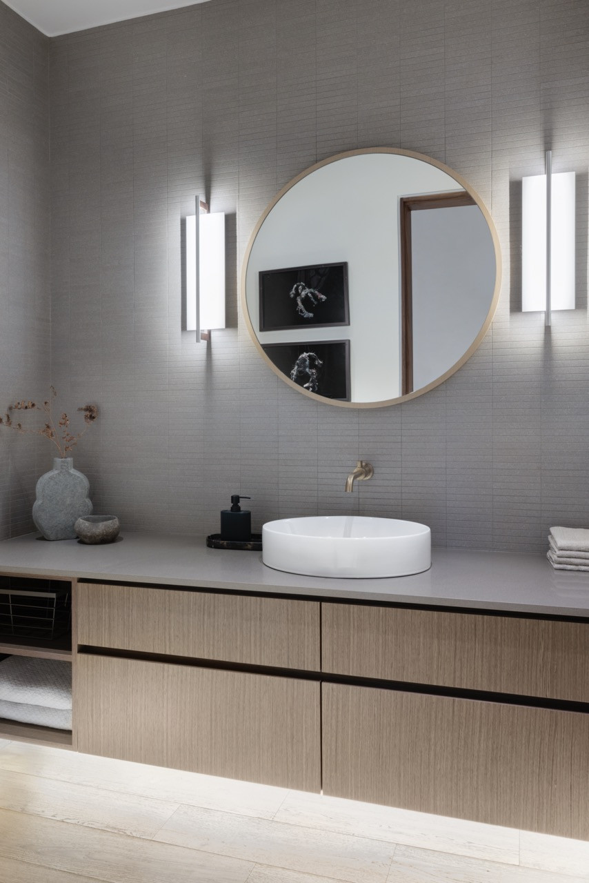 The primary bathroom features custom wood vanities with circular mirrors, demonstrating the warm material palette of browns and beiges chosen to reflect Vancouver's natural environment