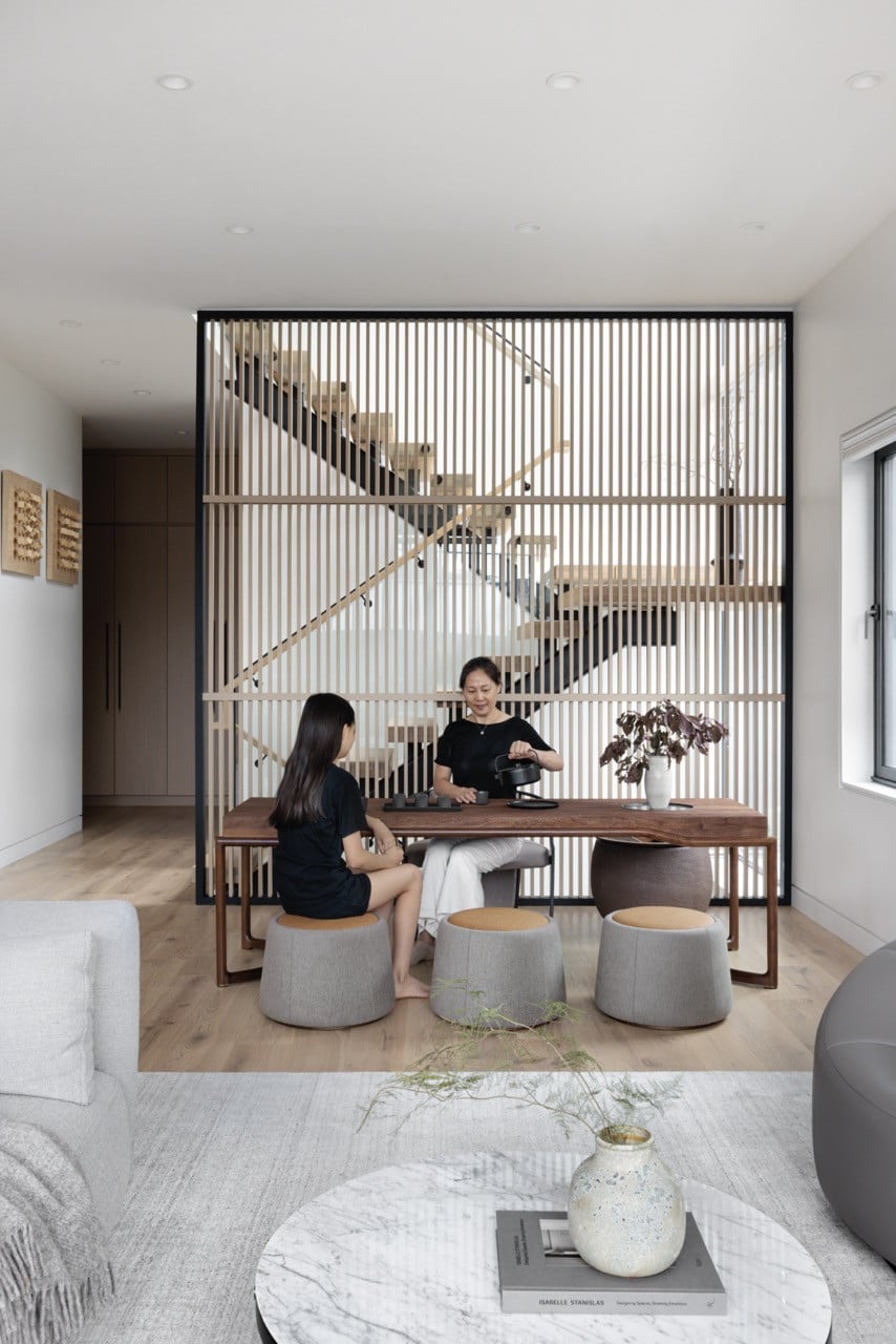 The tea table area demonstrates how the wood slatted walls create intimate zones within the open floor plan, with family members using the space for daily rituals that connect to their Chinese heritage