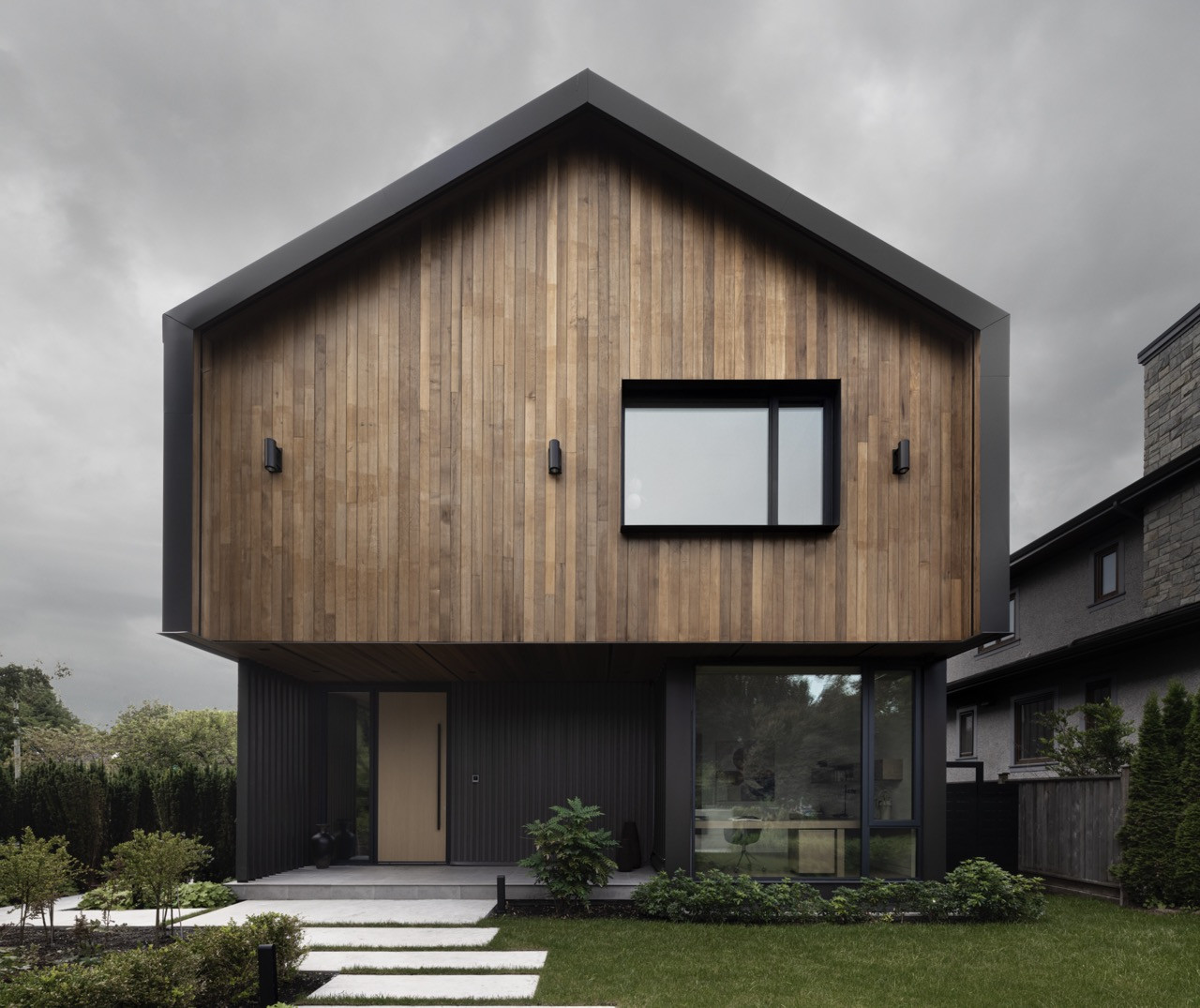 The front facade combines naturally stained cedar siding with dark metal cladding, creating a material contrast that reflects both the surrounding forest and Vancouver's weather conditions