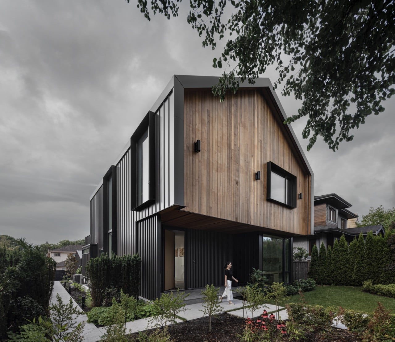 The house sits among mature trees in the Dunbar neighbourhood, with the naturally stained cedar siding blending with the surrounding forest while the standing seam metal roof provides weather protection