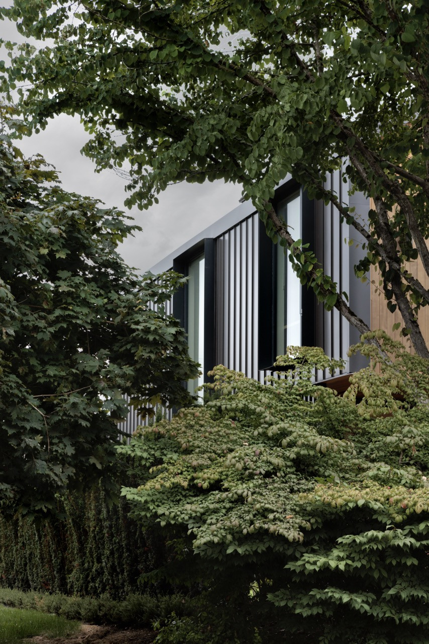 Dense landscaping frames views of the metal-clad portions of the house, demonstrating how the building materials respond to Vancouver’s rainy climate while integrating with the natural surroundings