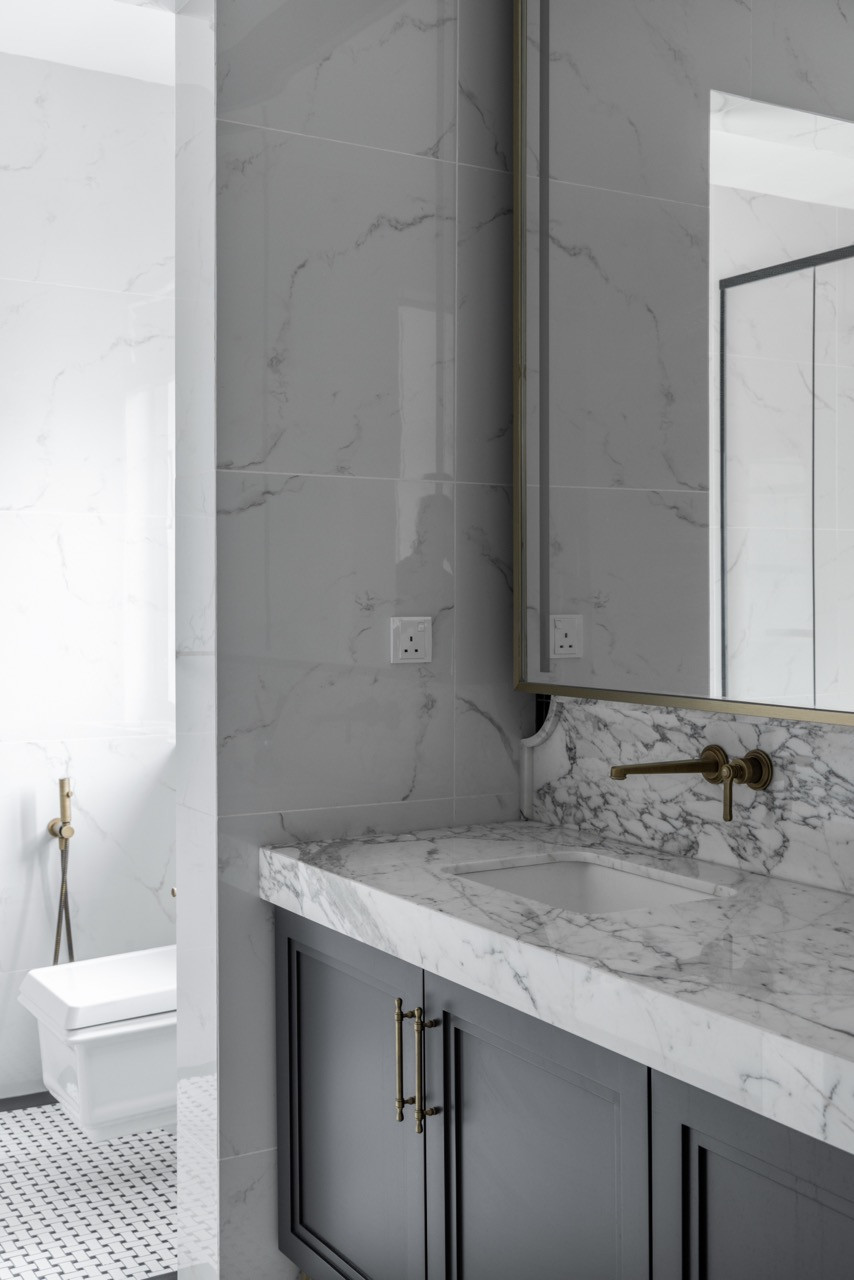 The master bathroom combines dark linear tiles with white marble surfaces, brass fixtures, and black-and-white mosaic flooring