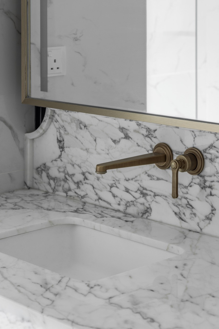 The master bathroom combines dark linear tiles with white marble surfaces and brass fixtures