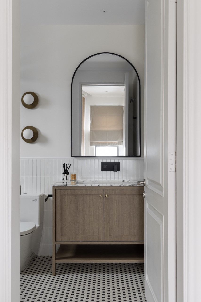 A ground-floor powder room showcases the home’s transitional design approach with vertical subway tiles, brass fixtures, and an arched mirror that echoes the exterior’s architectural language