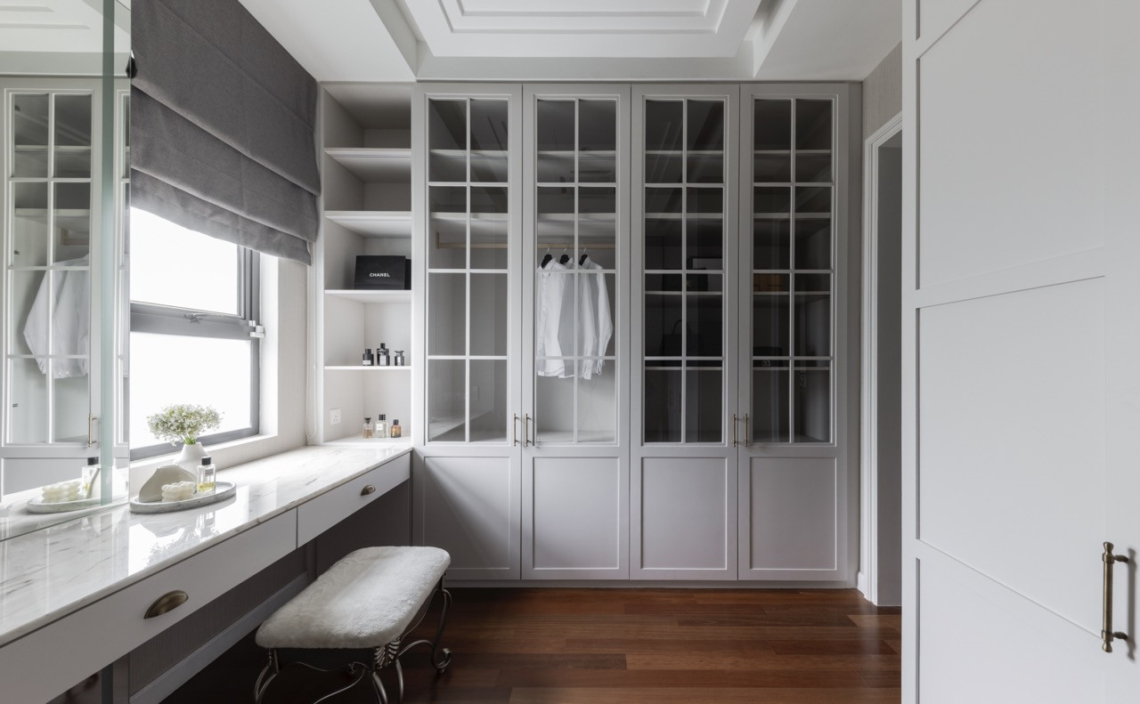 The dressing room employs floor-to-ceiling storage with glass-fronted cabinetry, coffered ceiling details, and a marble-topped vanity area