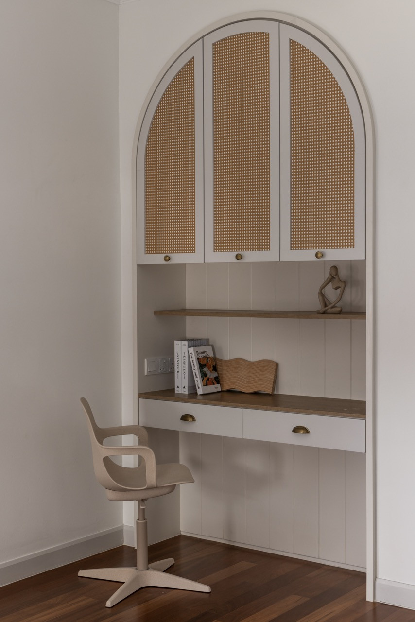 An arched desk nook demonstrates the thoughtful integration of functional spaces, featuring cane webbing cabinet doors and brass hardware that maintain the home's refined material palette