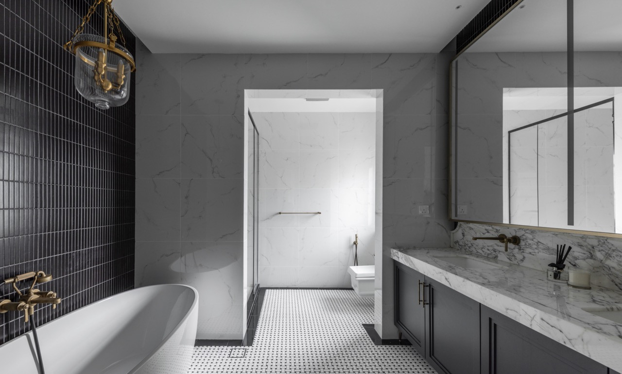 The master bathroom features a combination of dark linear tiles with white marble surfaces, brass fixtures, and black-and-white mosaic flooring. A freestanding tub anchors the space beneath a period-style brass and glass pendant light
