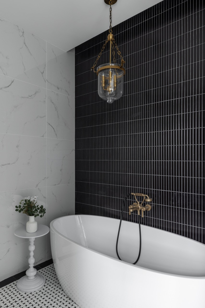 In the master bathroom, a freestanding tub anchors the space beneath a period-style brass and glass pendant light