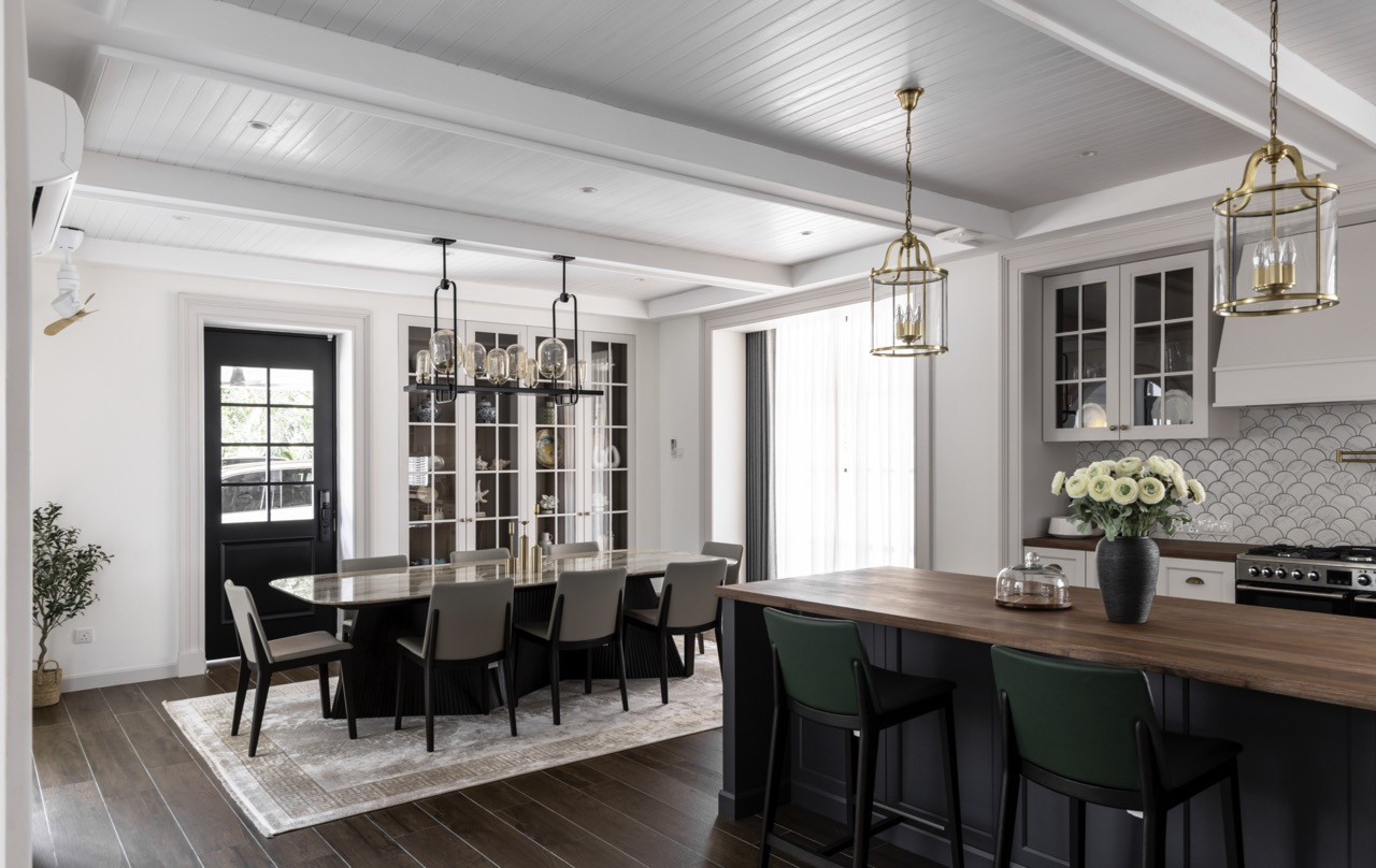Mermaid scale tile backsplashes provide geometric texture, and brass lantern pendants illuminate both cooking and dining areas beneath coffered ceiling details