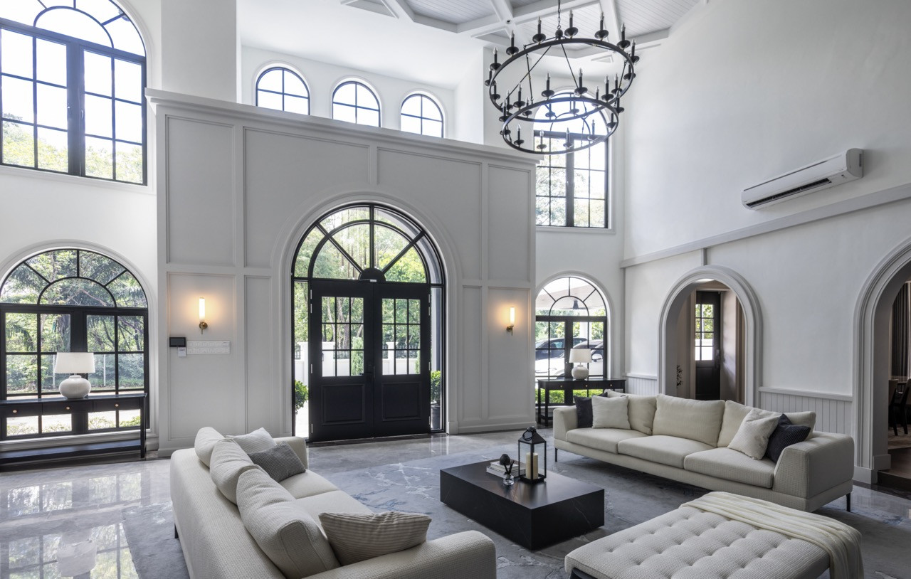 The double-height living space features coffered wood ceilings and a white brick fireplace wall, with neutral furnishings introducing comfort beneath the cathedral-like proportions