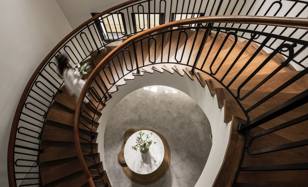 The sculptural spiral staircase with rich wooden treads and sleek black balustrade serves as both circulation and centrepiece, introducing movement and drama to the home's core while continuing the dialogue of contrast and refinement throughout the residence