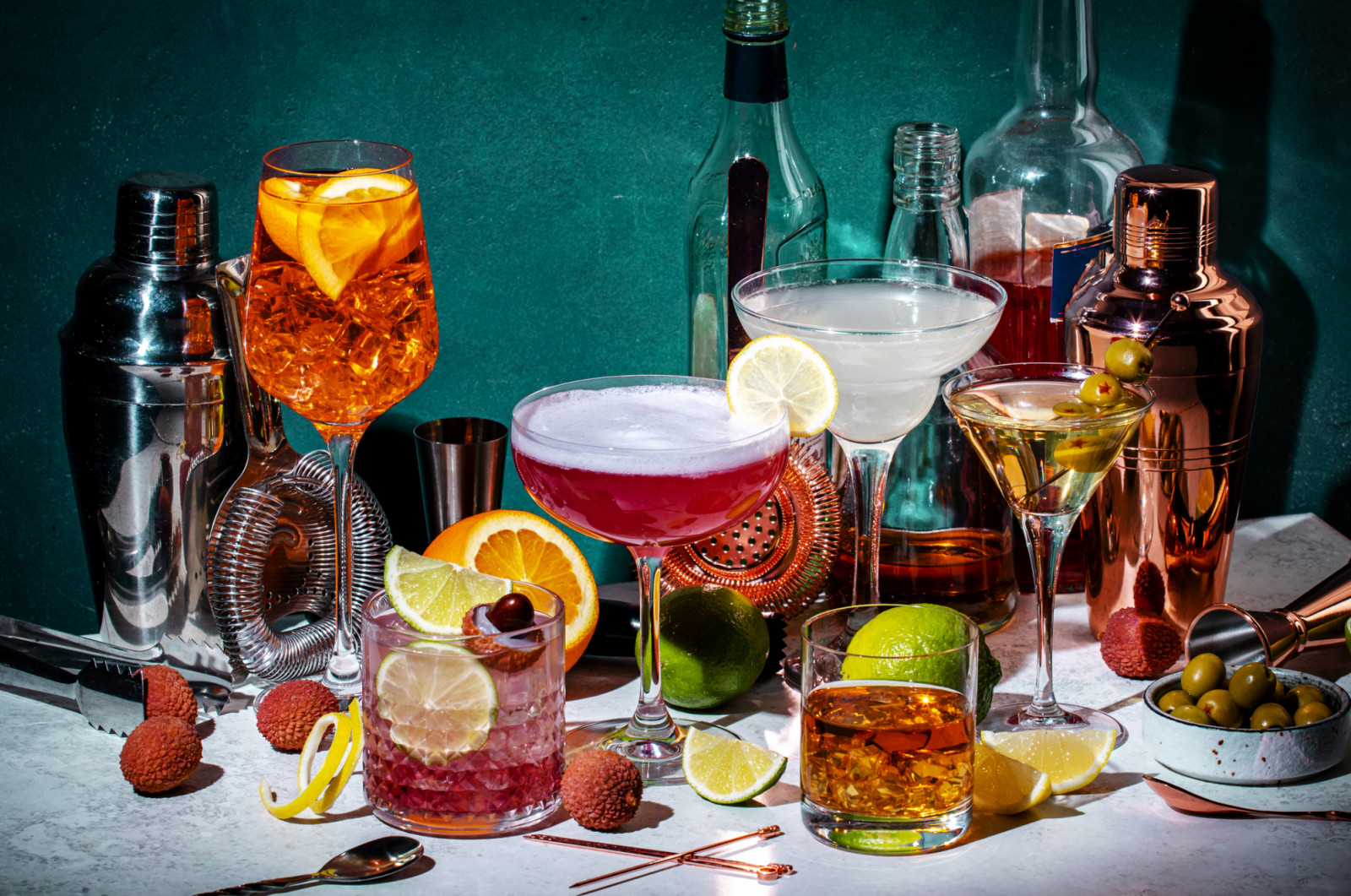 Cocktails. Strong drinks and aperitifs, bar tools, bottles on dark green background, hard light