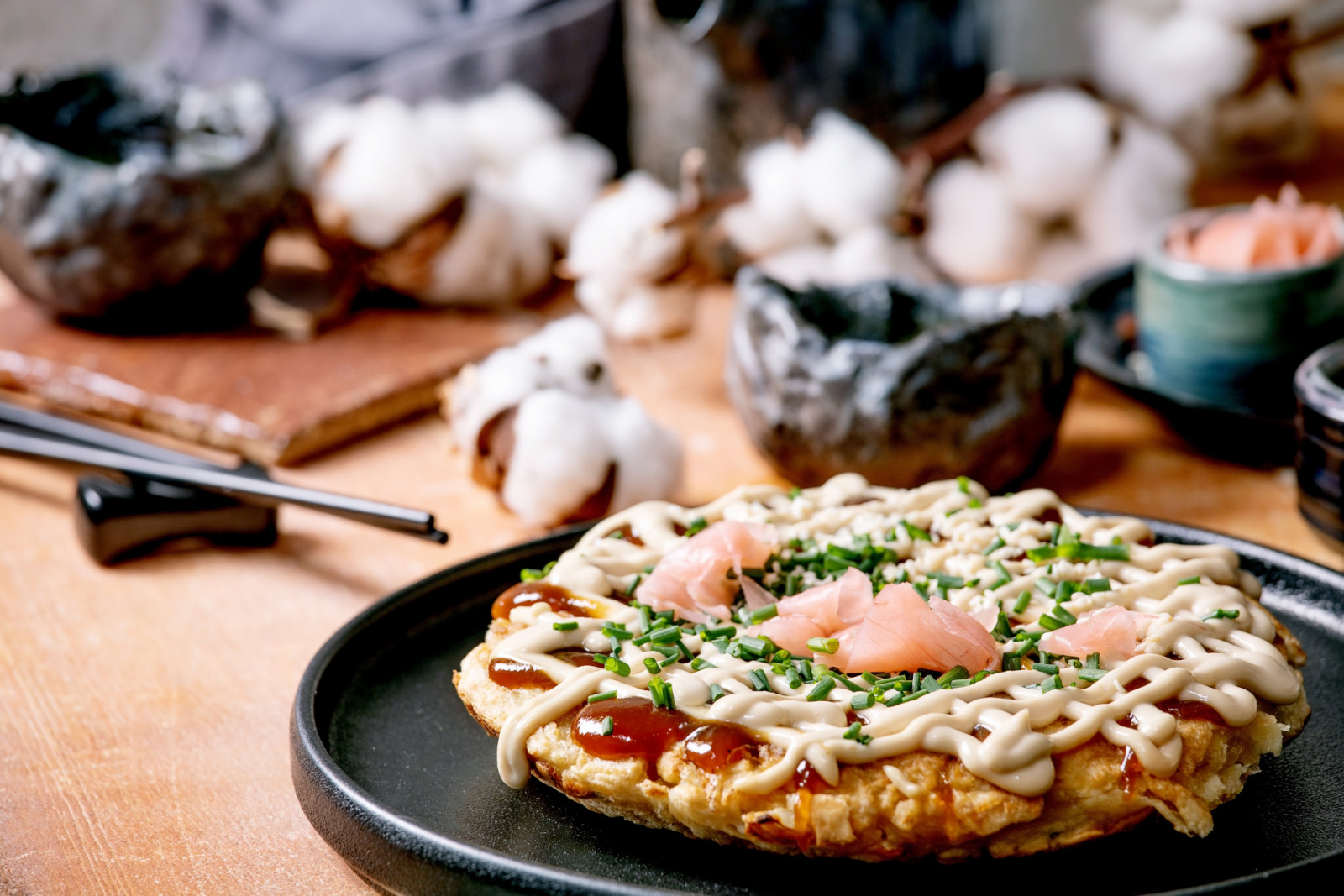 Homemade japanese fast food okonomiyaki cabbage pancake with onion. pickled ginger. mayo sauce on black ceramic plate. Chopsticks. teapot. cotton. ingredients above. Texture background. Flat lay. (Photo by: Natasha Breen/REDA/Universal Images Group via Getty Images)