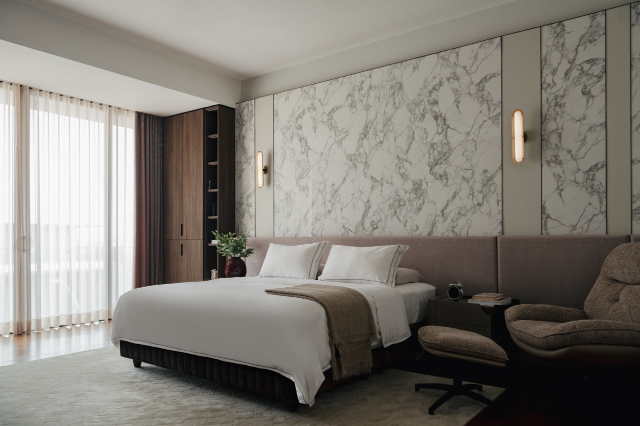 The master bedroom has marble-clad walls creating visual weight against the textured fabric headboards.