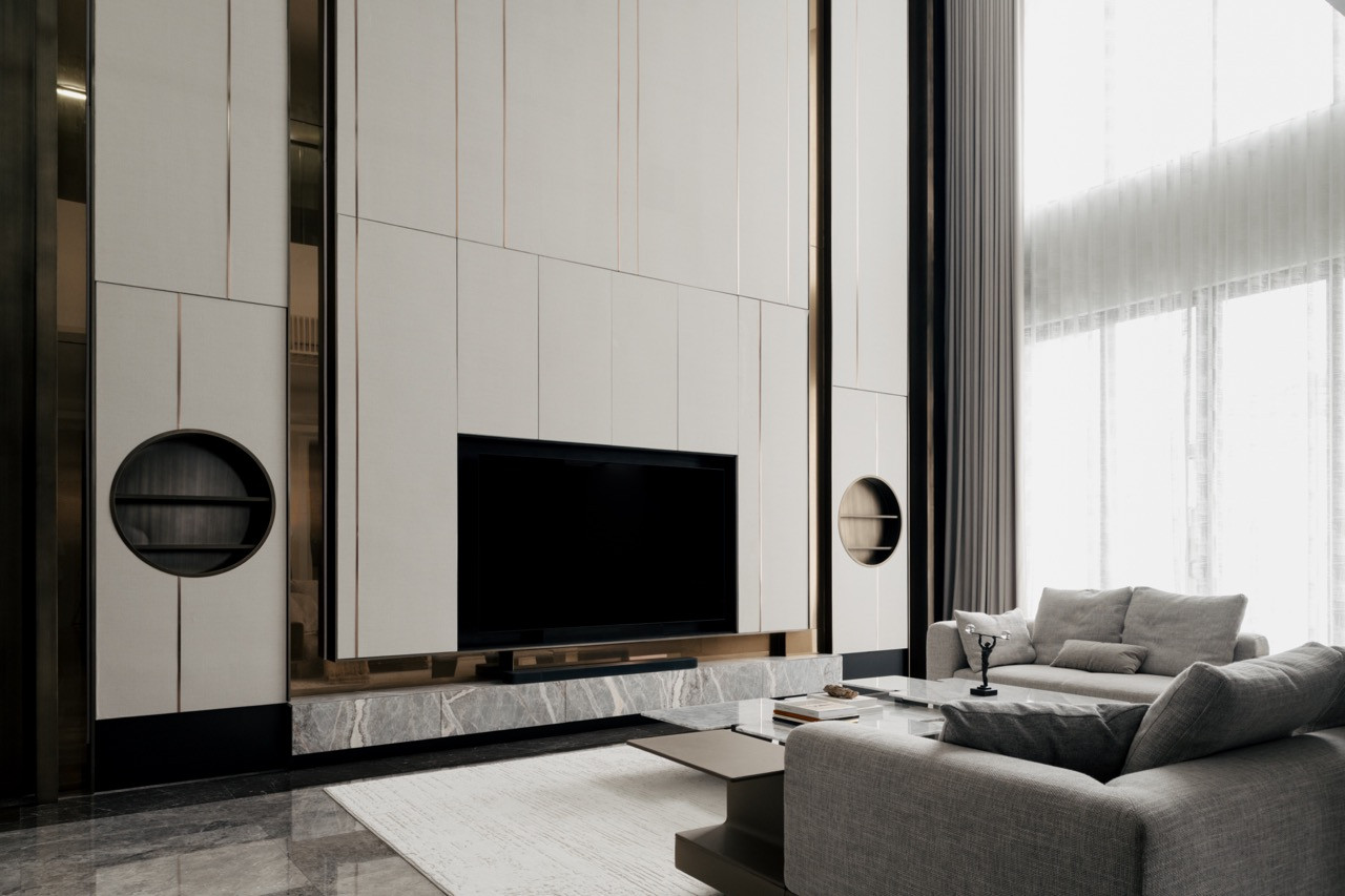 The main living area features the television wall with custom storage solutions and bronze accents that unify the material palette