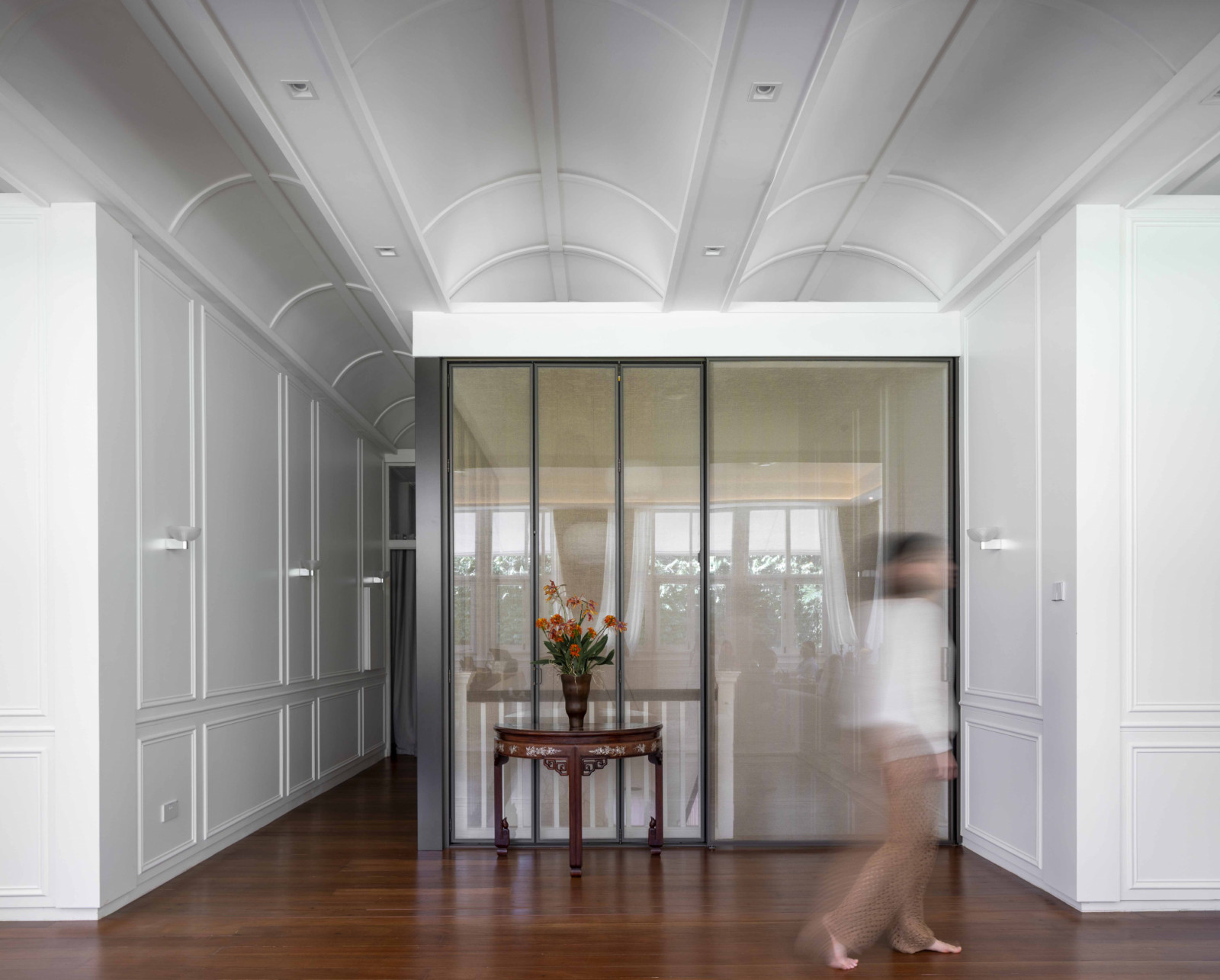 The staircase is encased in a glazed curtain wall that folds away to open or enclose the space as needed. Above it, a curving false ceiling was engineered to integrate seamlessly with the conserved structure