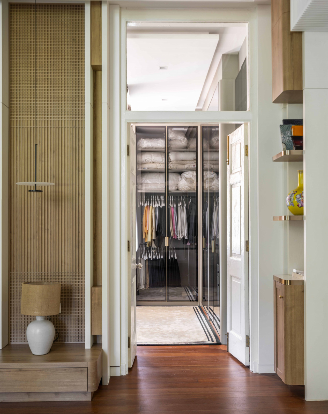 A view from the bedroom into the walk-in wardrobe reveals a seamless continuity of white and warm wood finishes