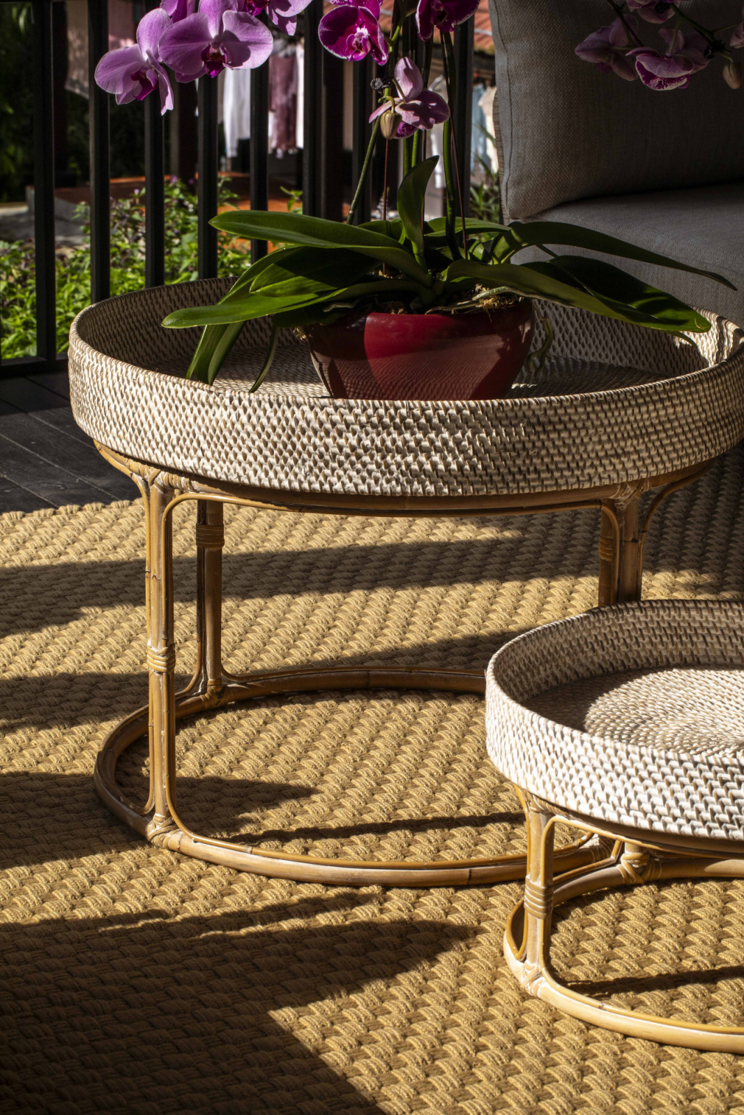 Morning light spills across the balcony, catching the woven textures of the rug and low tables in warm relief
