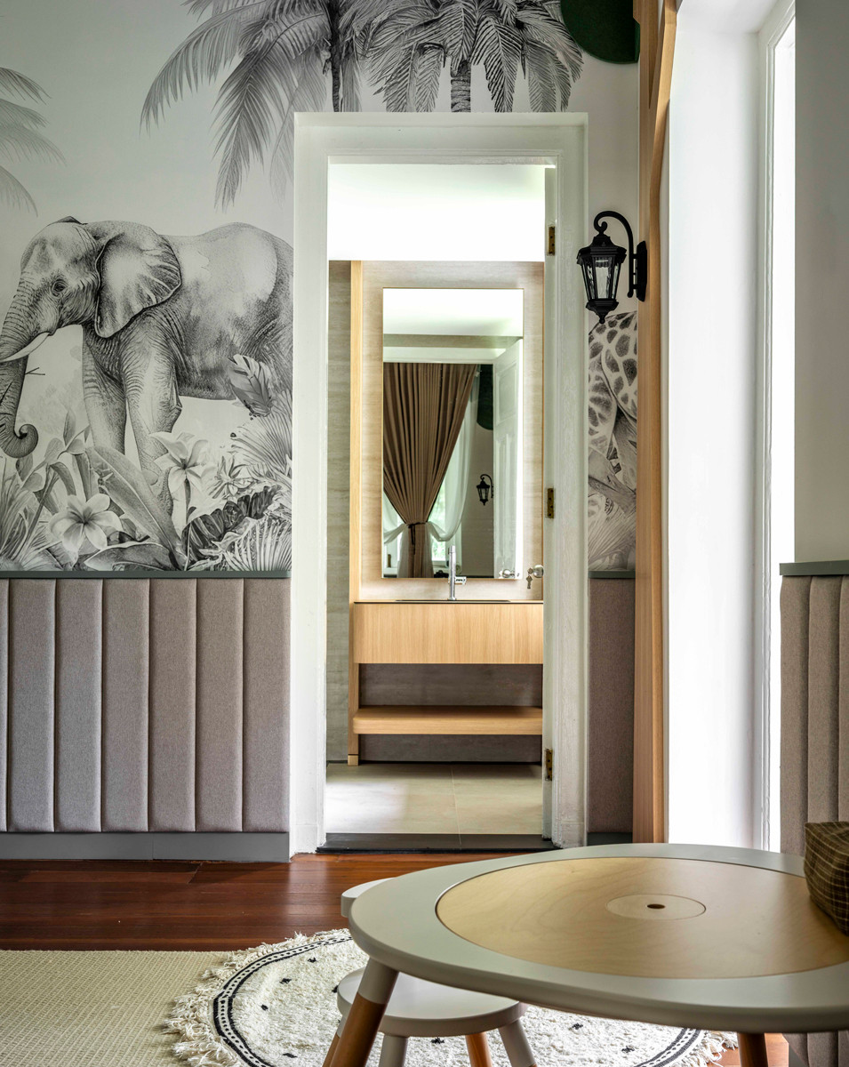 A view into the nursery’s bathroom framed by walls adorned with black-and-white wallpaper featuring hand-drawn safari illustrations