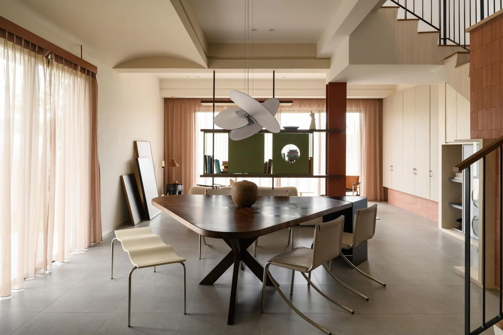 Floor-to-ceiling windows flood the dining space with natural light, while the sculptural pendant light creates visual interest against the neutral design palette (Photo: TWJPTO)