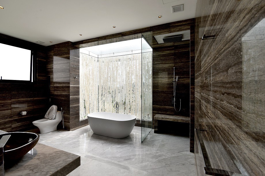 The master suite bathroom features a freestanding tub within a glass enclosure, surrounded by board-formed concrete walls and timber ceilings that frame views of the landscape