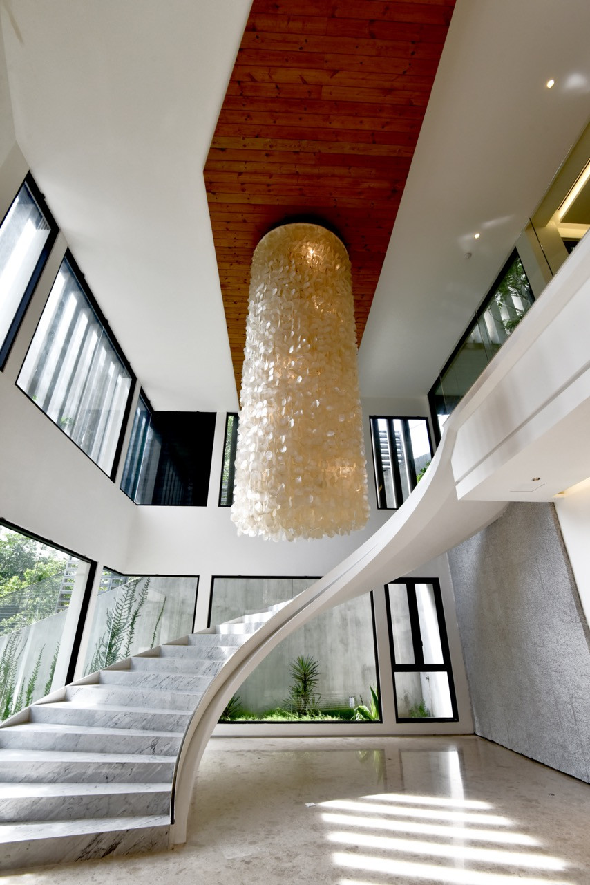 The sculptural marble staircase curves upward through the double-height foyer, with a large shell-inspired chandelier