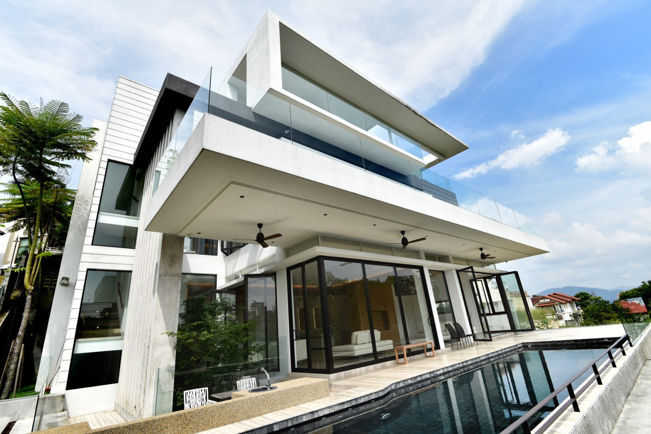 The house's angular concrete geometry creates dramatic overhangs and deep shadows, while large glazed openings maintain visual connection to the forest canopy.