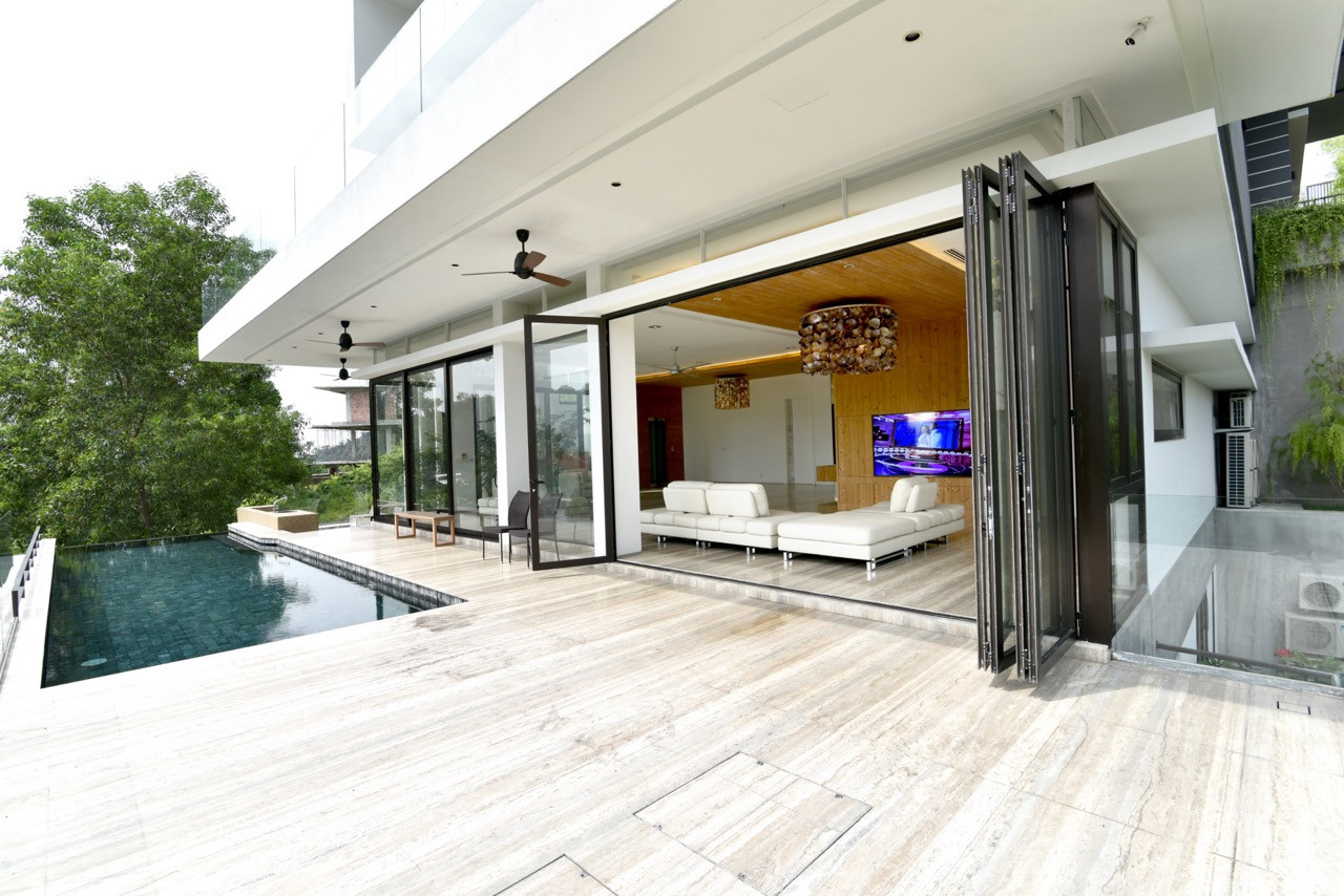 Folding glass doors completely open the interior to the pool deck, with the timber ceiling extending outward to create covered outdoor living areas
