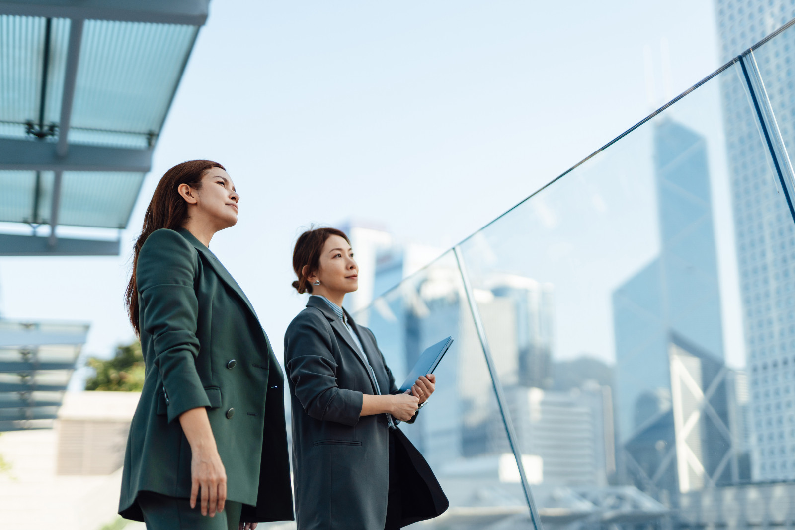 Two thoughtful Asian colleagues holding laptop, looking at cityscapes, feeling optimistic and hopeful about the future. Teamwork and collaboration. Women's empowerment and career achievement. (ภาพ: Oscar Wong via Getty Images)