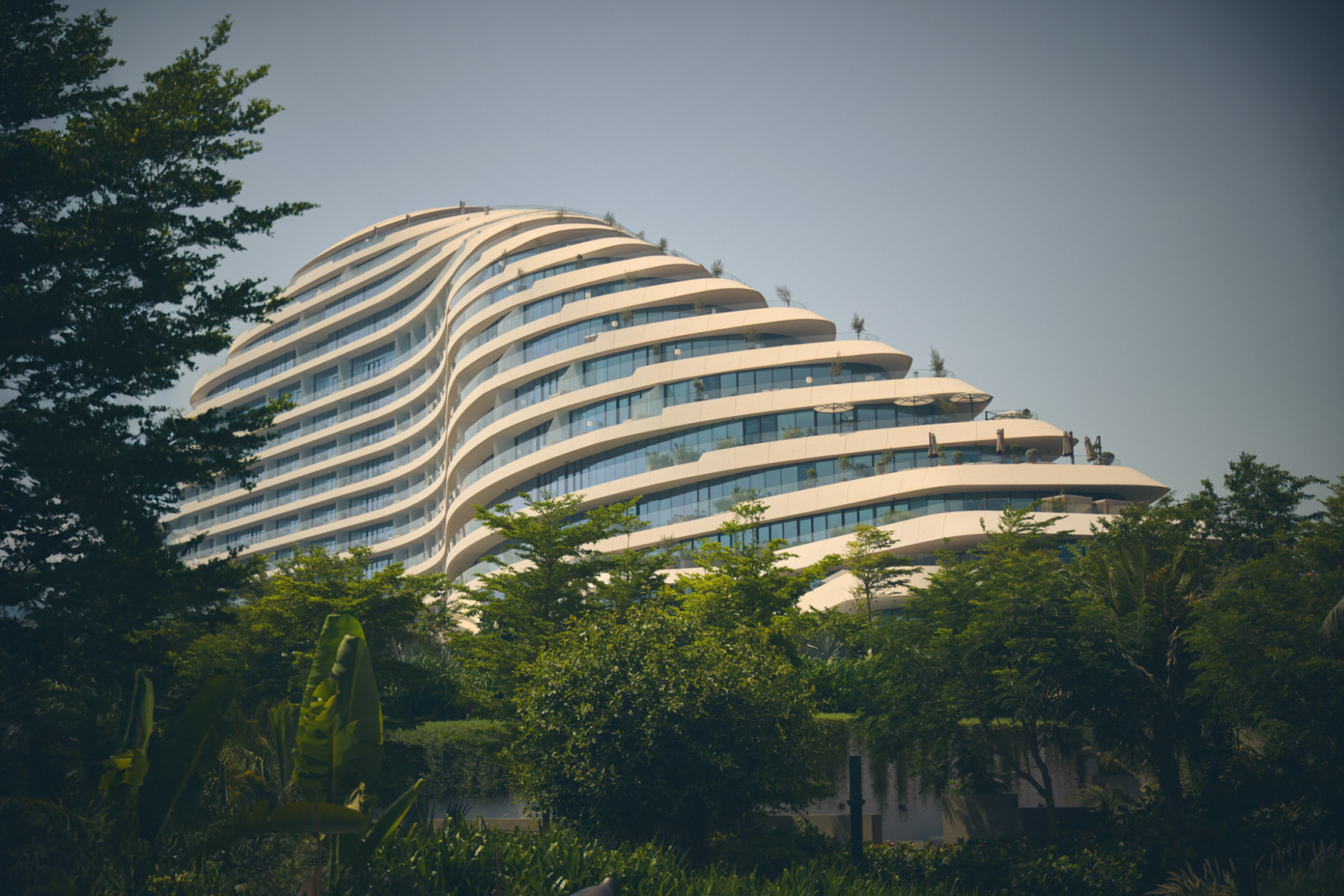 Jumeirah Marsa Al Arab’s distinctive curved facade rises from lush tropical gardens, its horizontal balconies creating a rhythmic pattern that echoes the movement of ocean waves