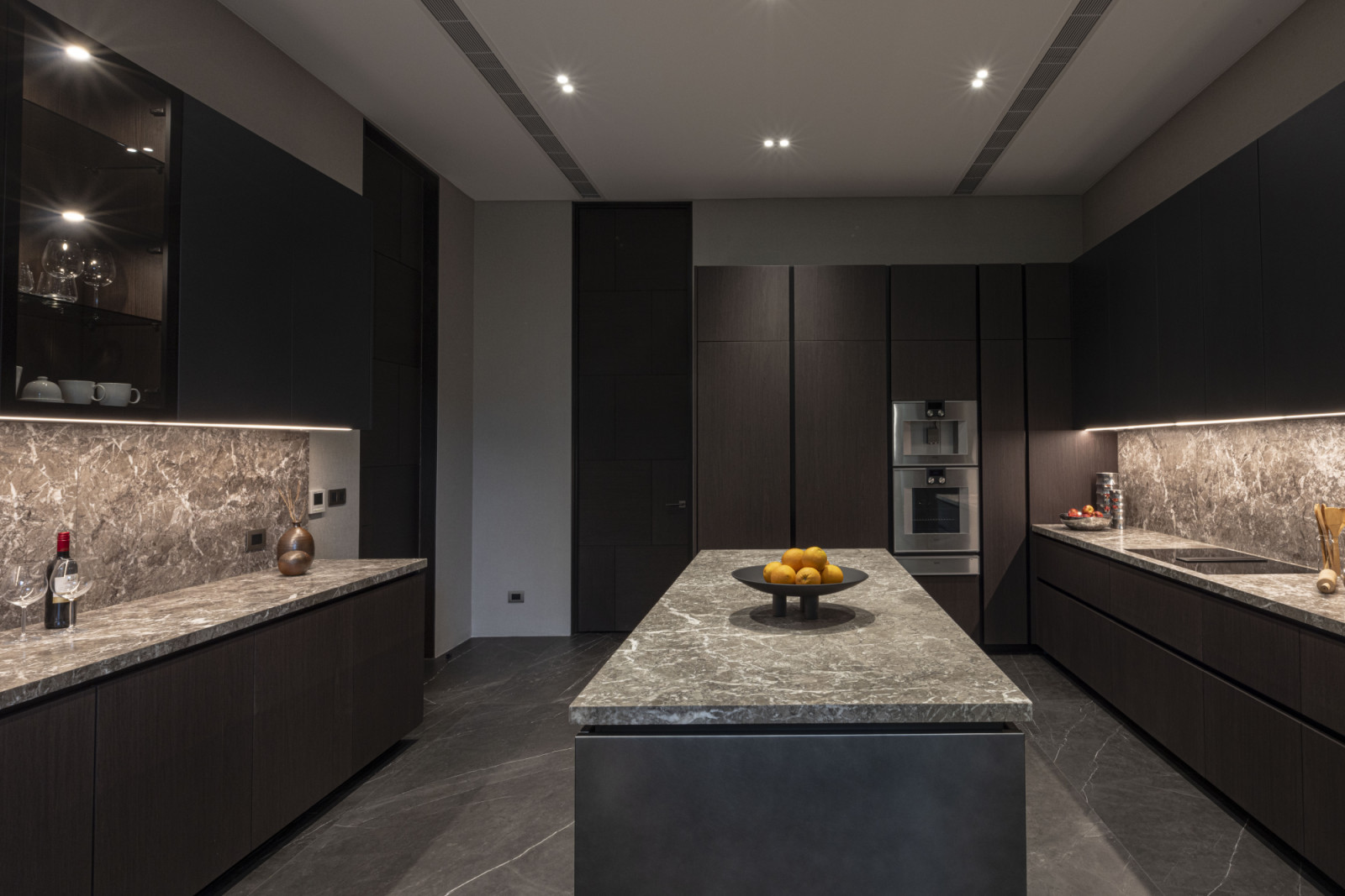 A sculptural island grounds the space, thanks to its titanium-toned lacquered fronts paired with a striking stone surface, to form a bold yet refined centrepiece