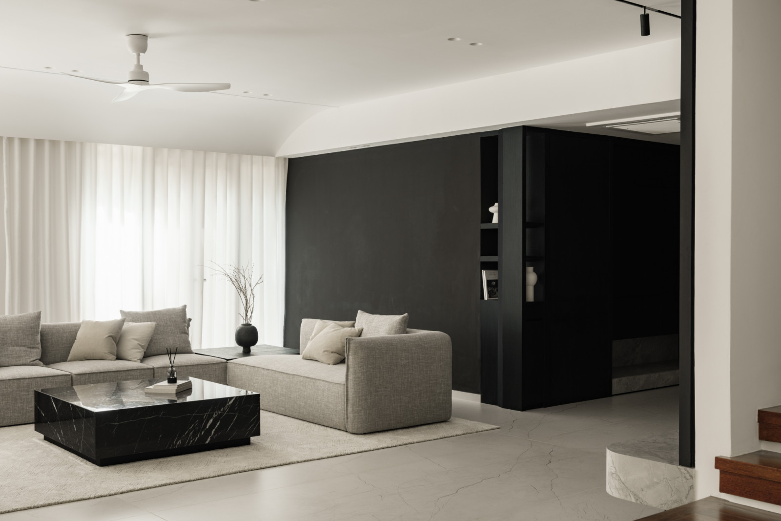 The living area's solid black feature wall creates depth and visual harmony, contrasting with the lighter dining and kitchen areas