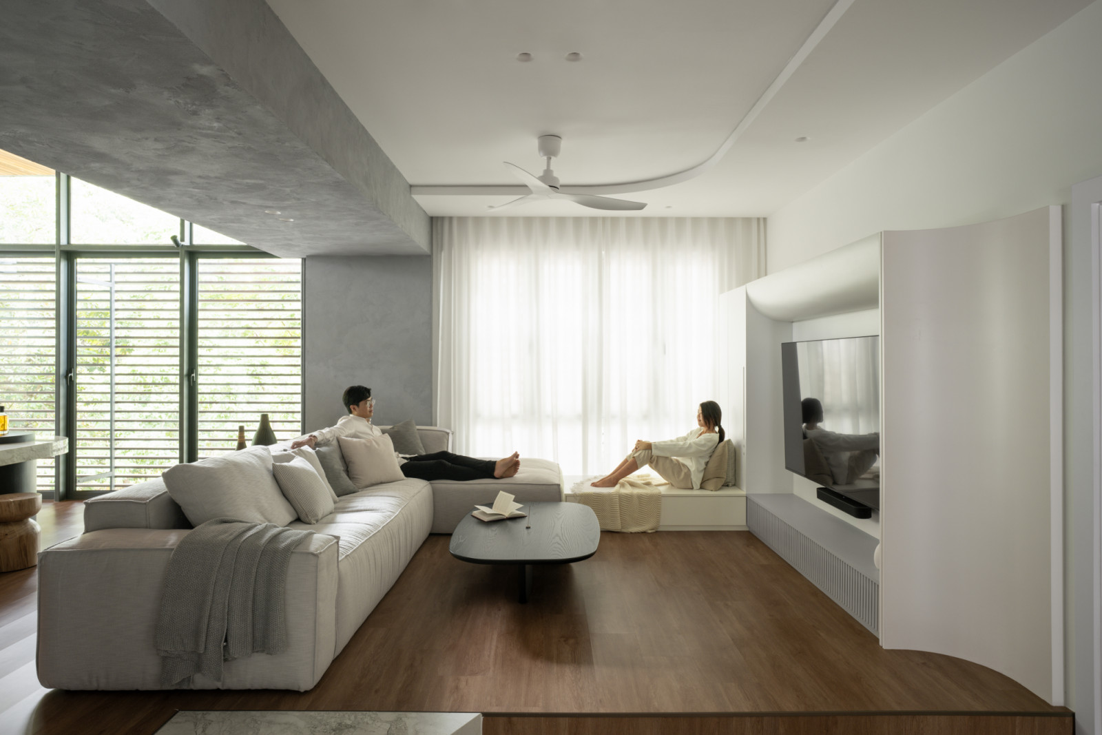 The upstairs living area features elegant wood flooring and modular grey seating, positioned to capture natural light from the expansive windows
